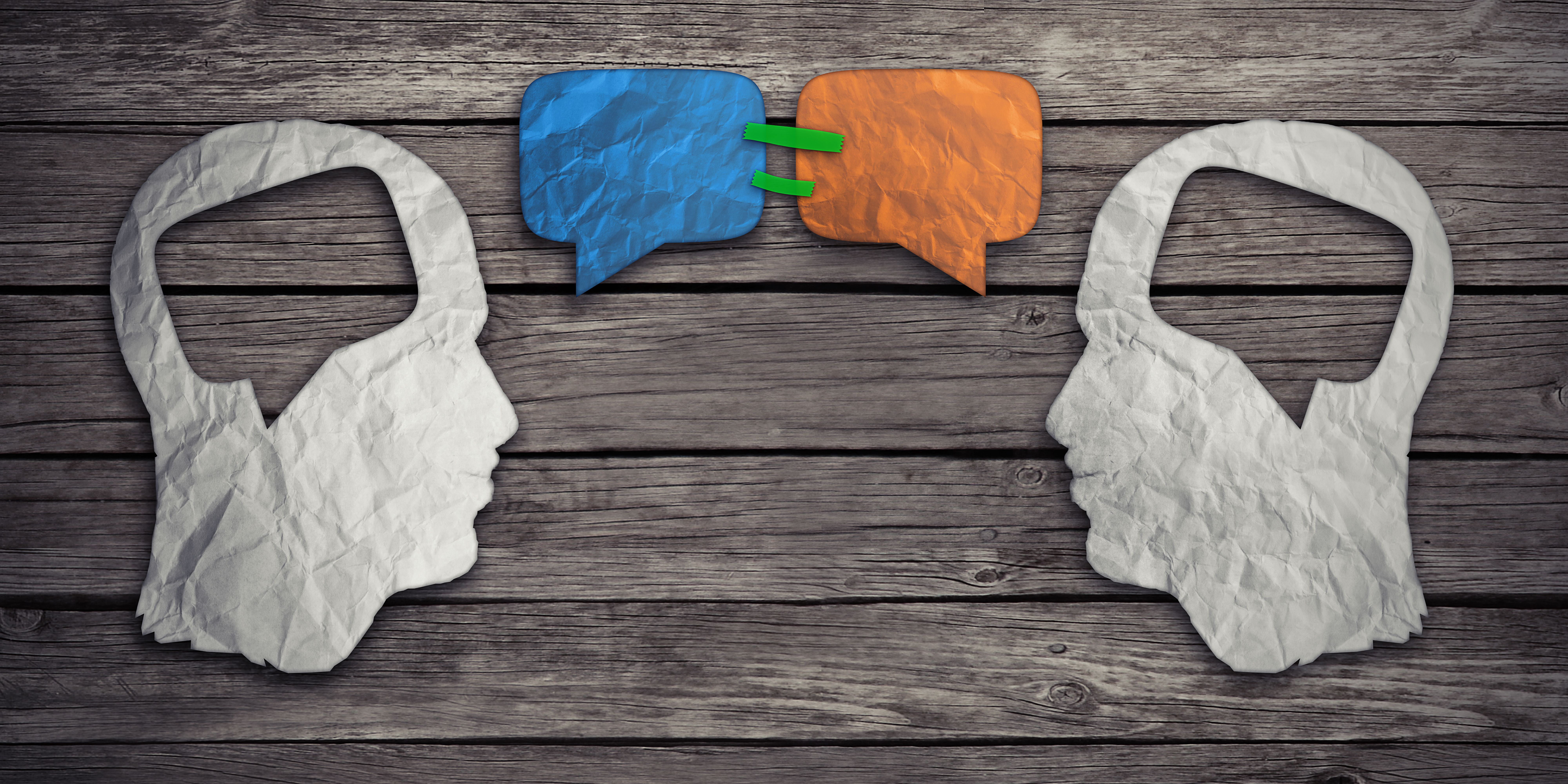 Speaking together social media concept as two crumpled pieces of paper shaped as human head with talk bubble icons taped as communication symbol for business compromise agreement